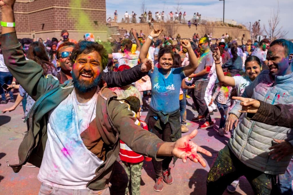 A group of people covered in colorful dust cheer with their arms in the air.