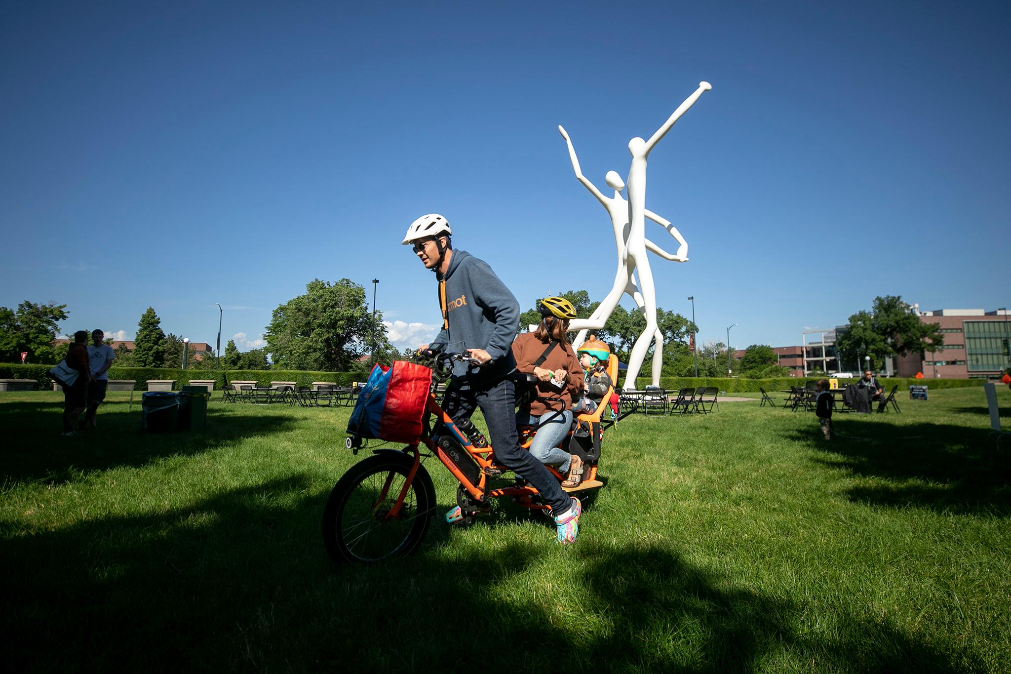 A family stands on an e-bike ready to go with a large white sculpture behind them.