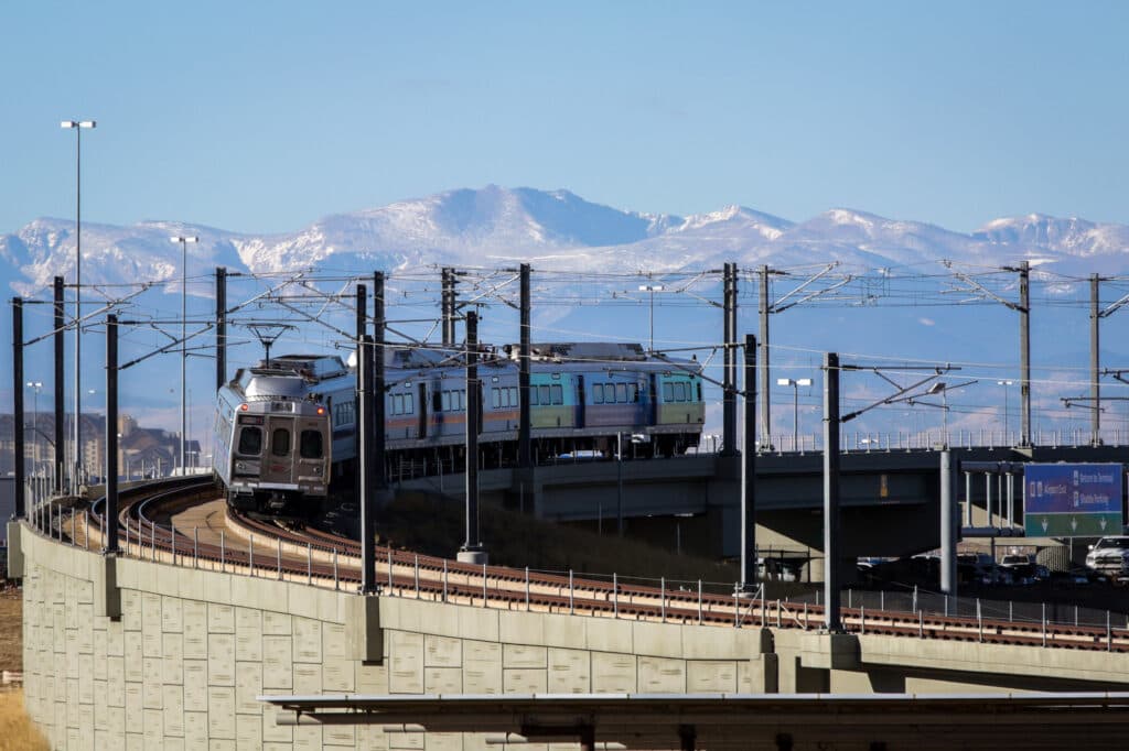 An RTD A Line commuter rail train on the track with the mountains in the background.