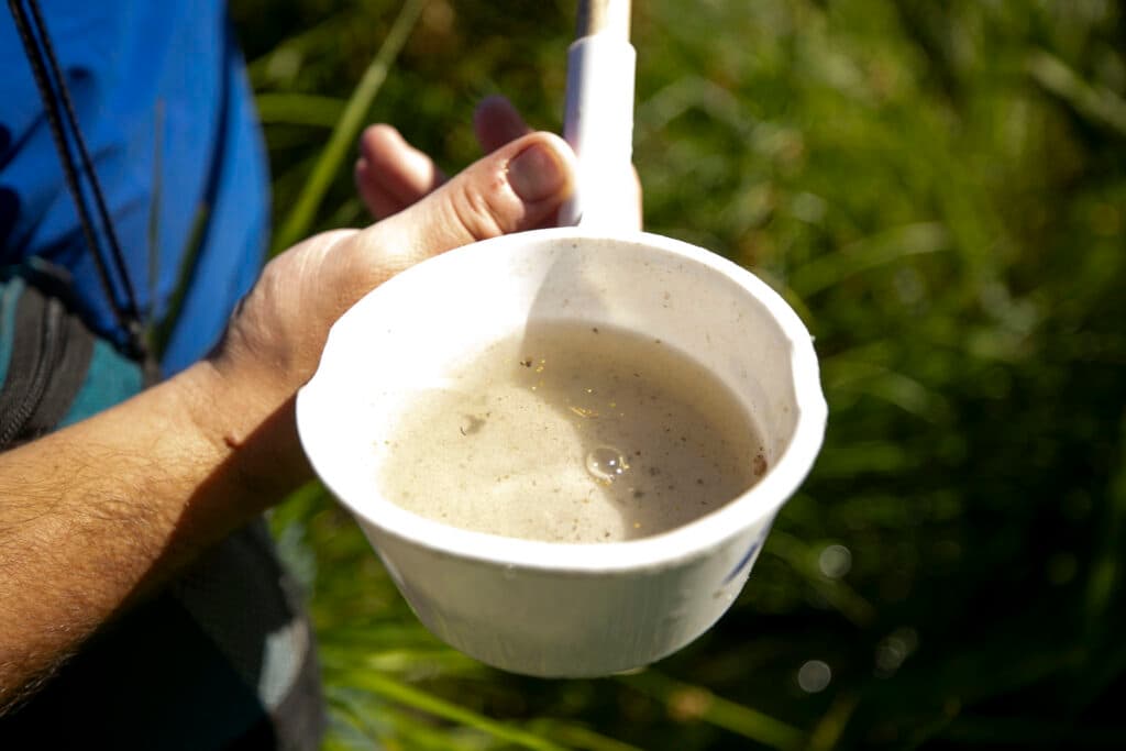 A plastic ladle is filled with brownish water and specs of dirt.