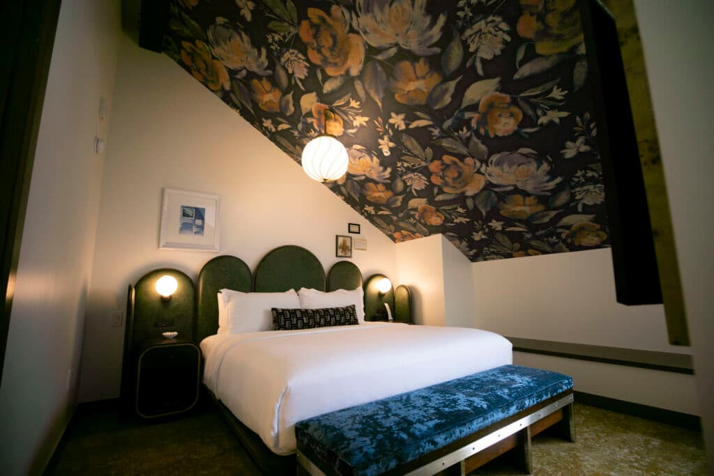 A neatly made hotel bed beneath a floral-patterned ceiling, ready for a guest.