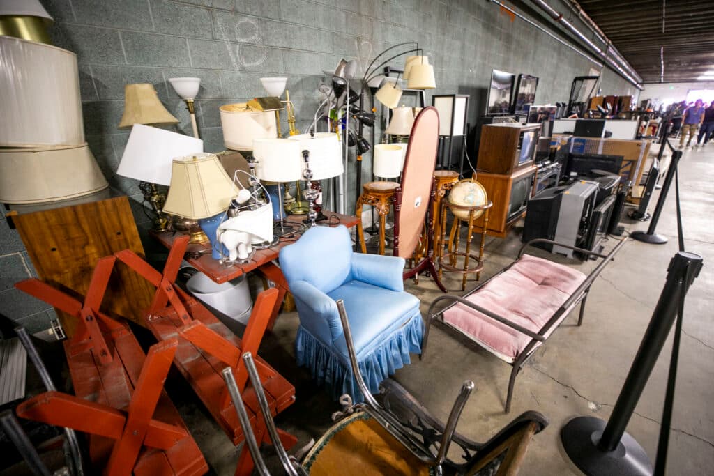 Chairs and mirrors and TVs and a globe and benches and more are clustered in a warehouse.