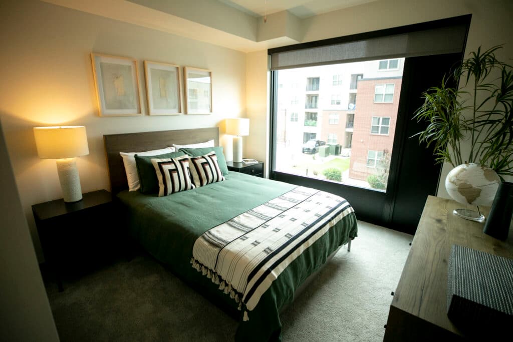 A bed with green covers in a warmly lit, modern room.