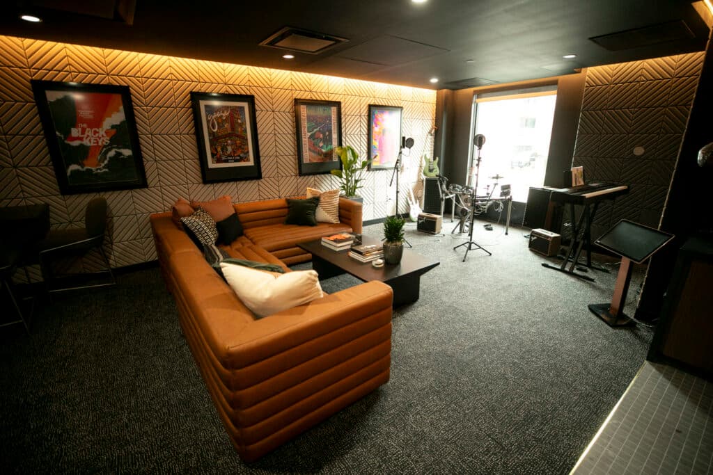 Studio mics, a drum set, keyboard and couches fill a warmly lit, sound-padded room.