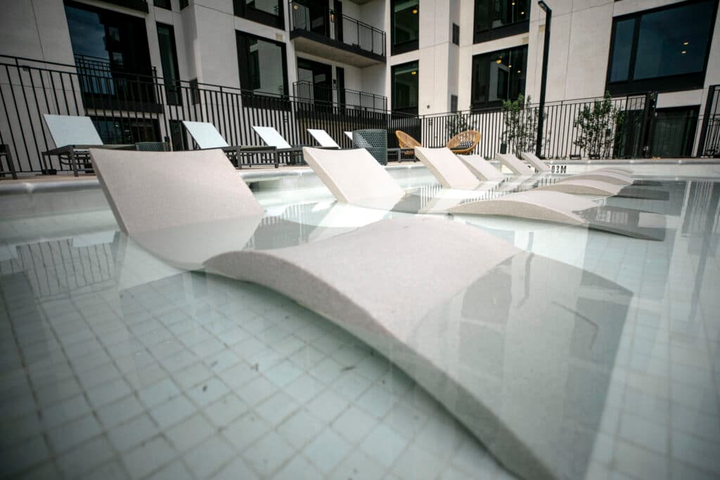 Reclining chairs are halfway submerged in a shallow section of a pool.
