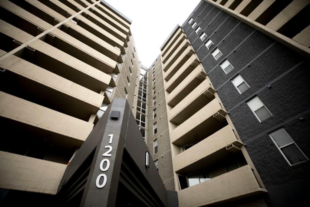A view looking up at a towering apartment building, complete with stacked terraces and big numbers that read &quot;1200.&quot;
