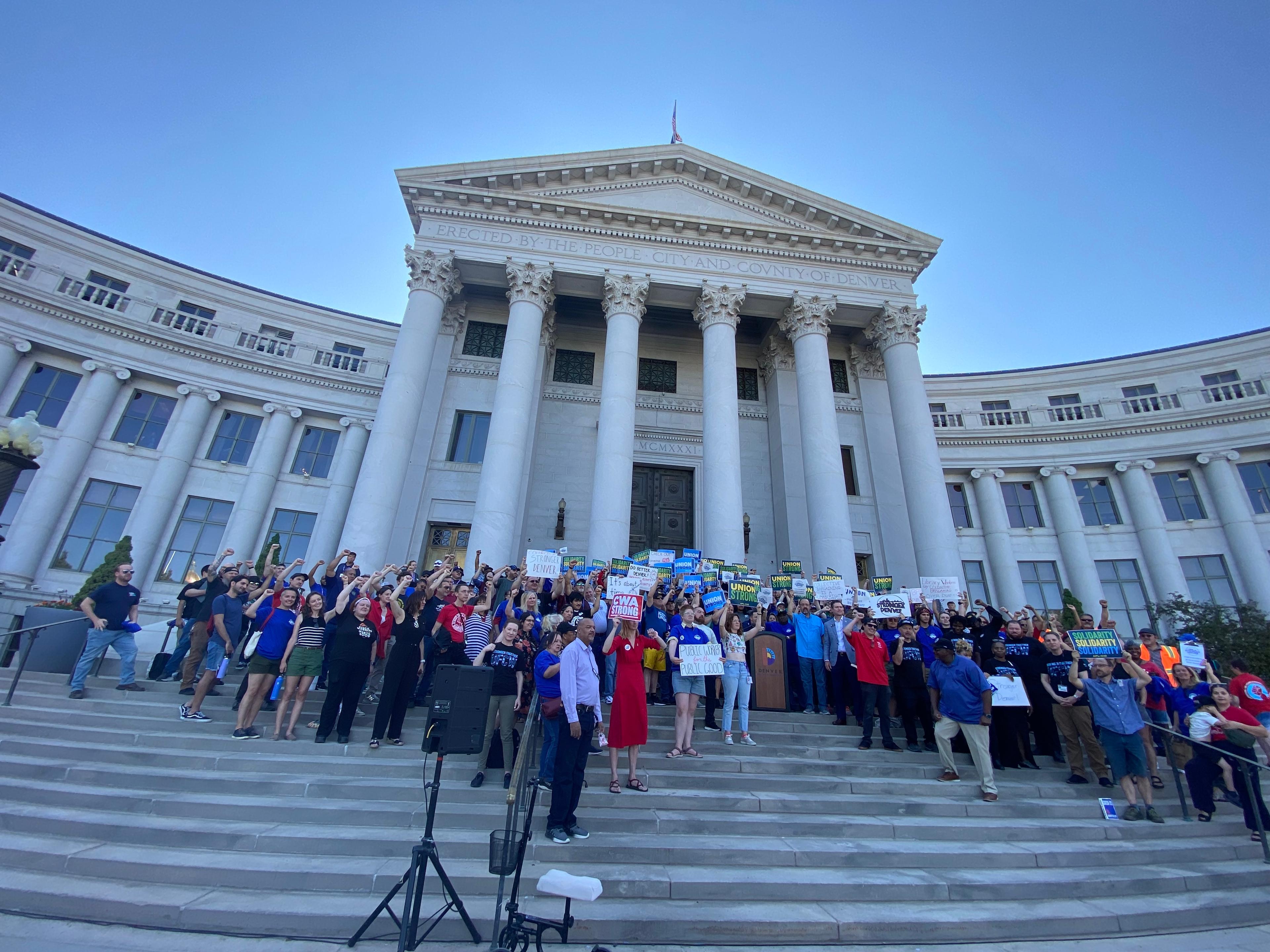 A crowd stands on the steps of the Denver City and County Building holding signs in support of collective bargaining for city employees.