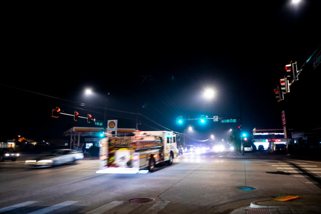 A fire truck drives through a big intersection; the lights around it streak with movement.