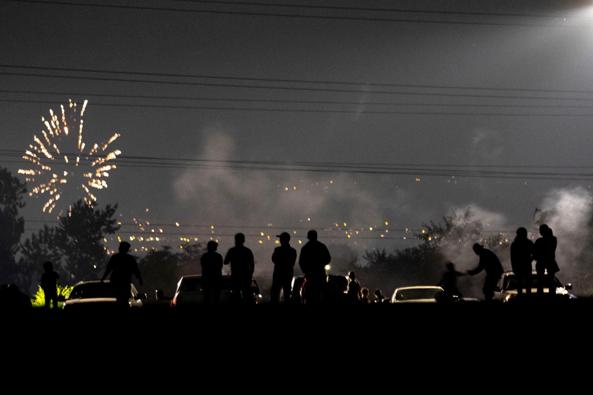 People are silhouetted as fireworks blow up in the background. The air around them is very hazy.