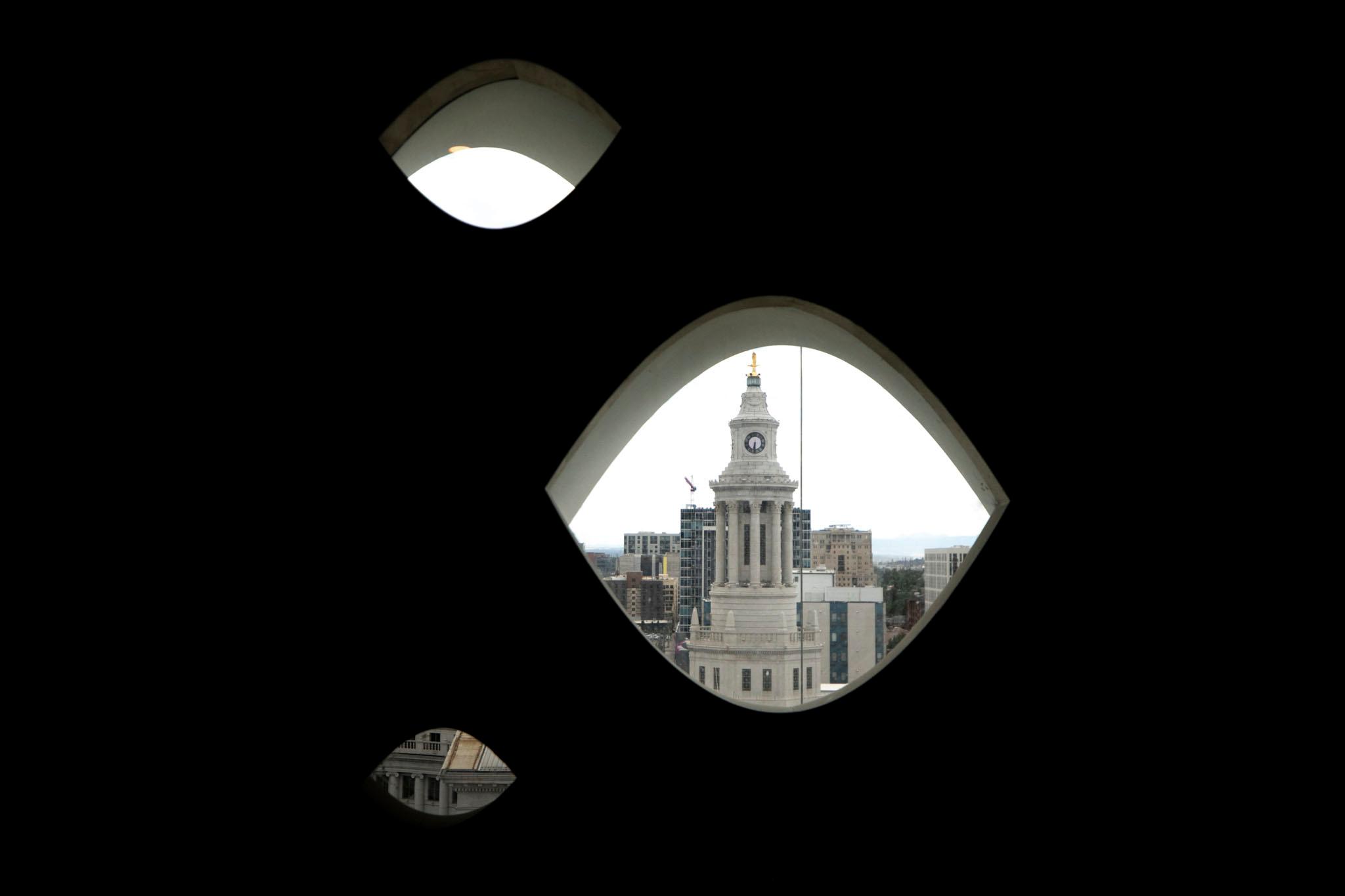 A stone clocktower is seen through one of three eyeball-shaped windows; the room inside is completely black.