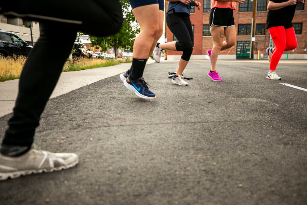 People in athletic outfits and multiple colors of shoes jog in place; their torsos are cut off by the top of the frame.