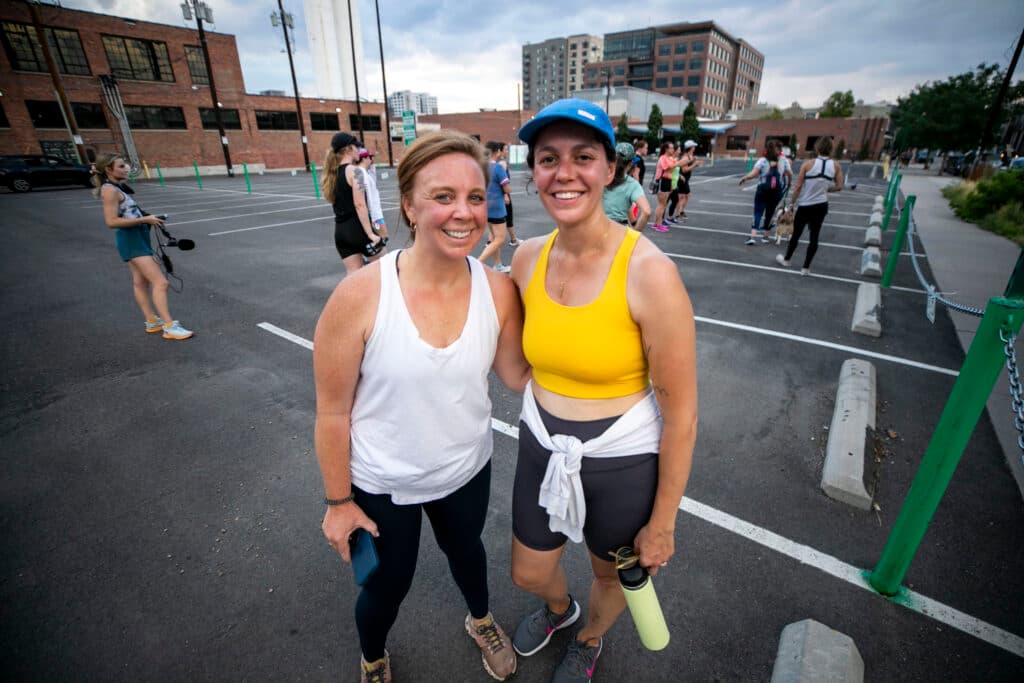 Two woman in athletic gear stand in a parking lot.