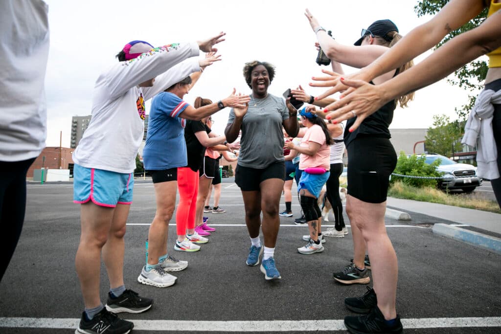 A woman in athletic gear runs through a row of people, applauding and high-fiving her as her smile beams in the center of the frame.