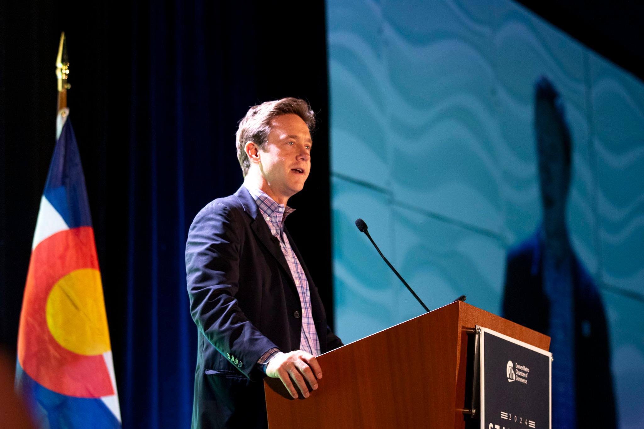 A man in a blue blazer speaks at a podium.