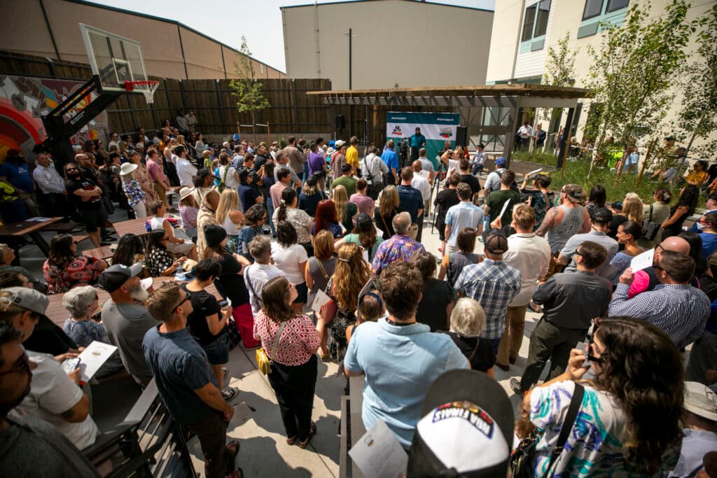 A large crown of people gather around a pergola on a patio.