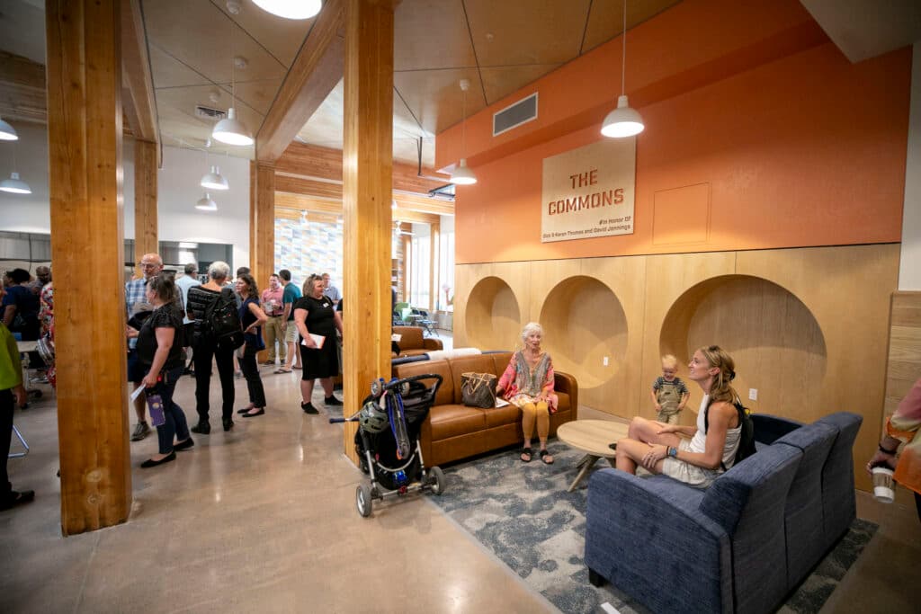 People mill around a warmly-lit room with a sign on the wall that reads &quot;The Commons.&quot;