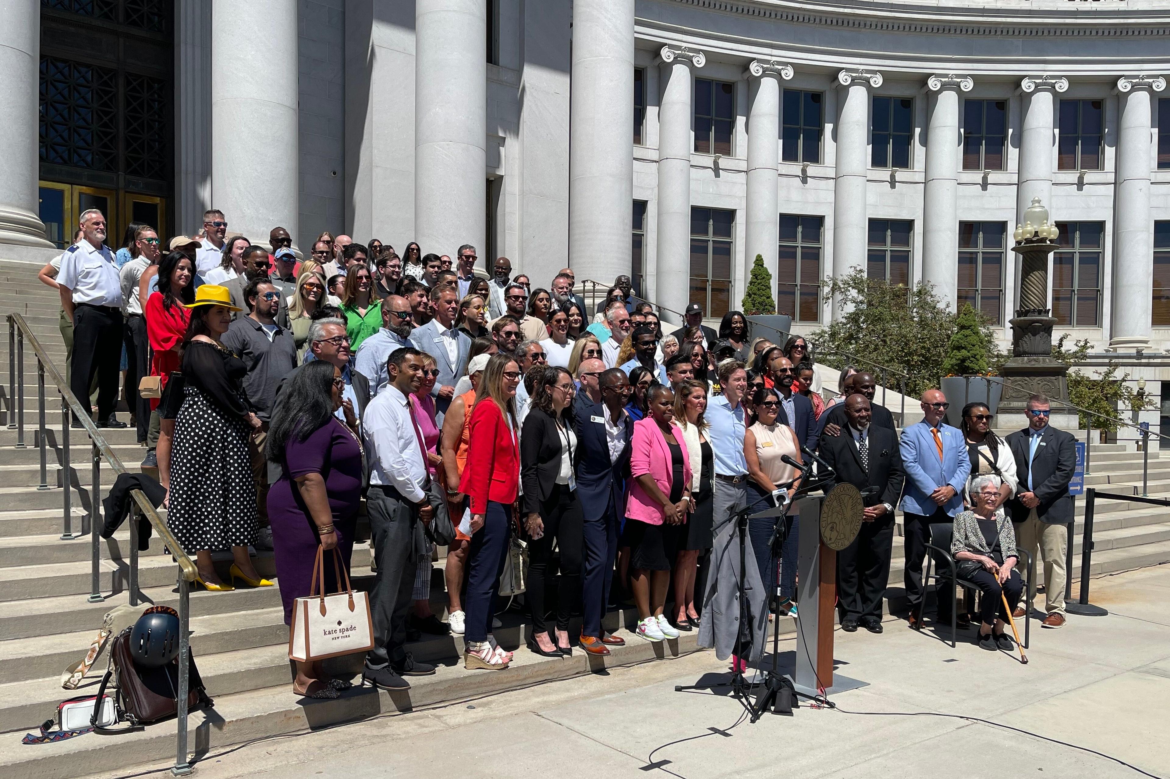 A group of politicians and nonprofit surround Mayor Mike Johnston on the steps of the City and County building as he announces a proposed sales tax to fund affordable housing.