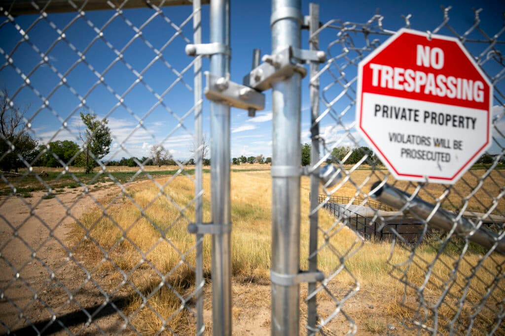 A fence is out of focus in the foreground, adorned with a sign that reads, &quot;NO TRESPASSING.&quot; Behind it is a mostly yellow field with some trees on the horizon.