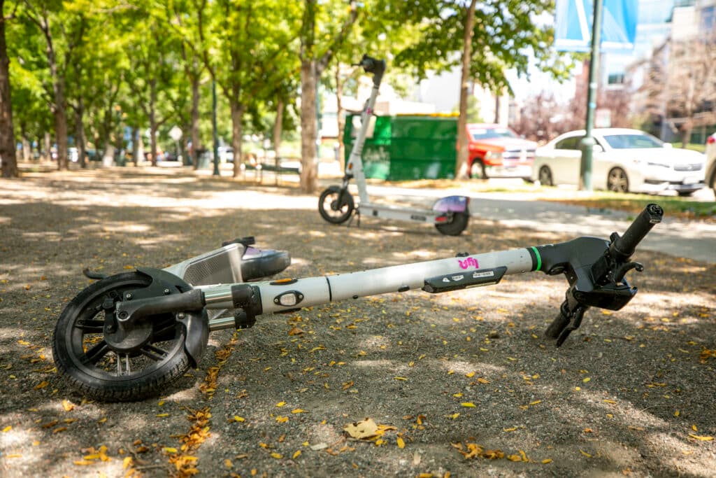 A white scooter is horizontal in the frame, lying on the ground with one upright in the background.