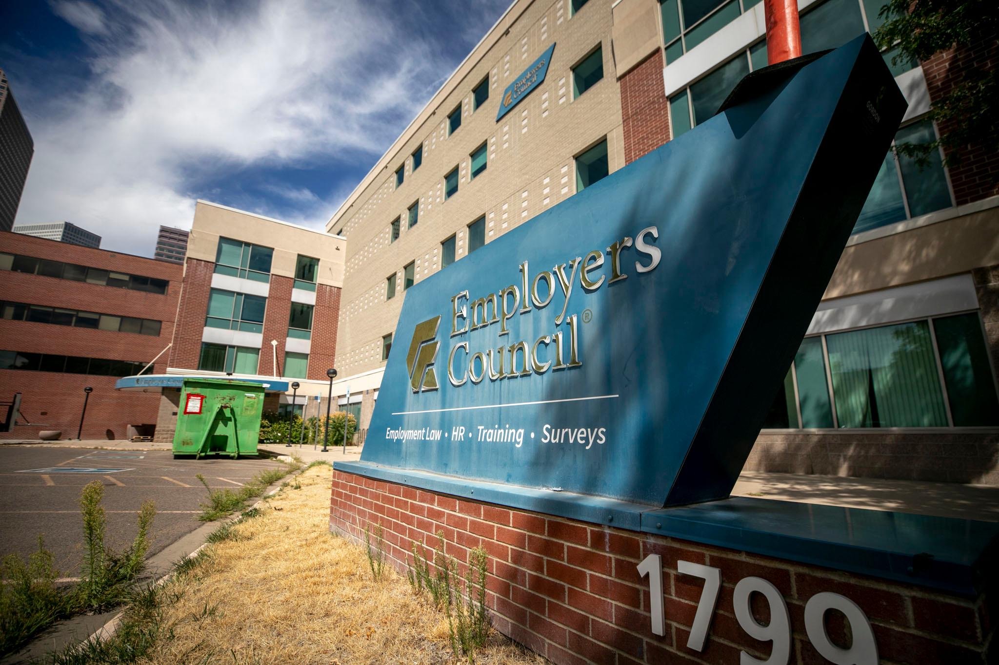 A red and tan brick building under a blue sky. A blue and white sign reads "Employers Council."