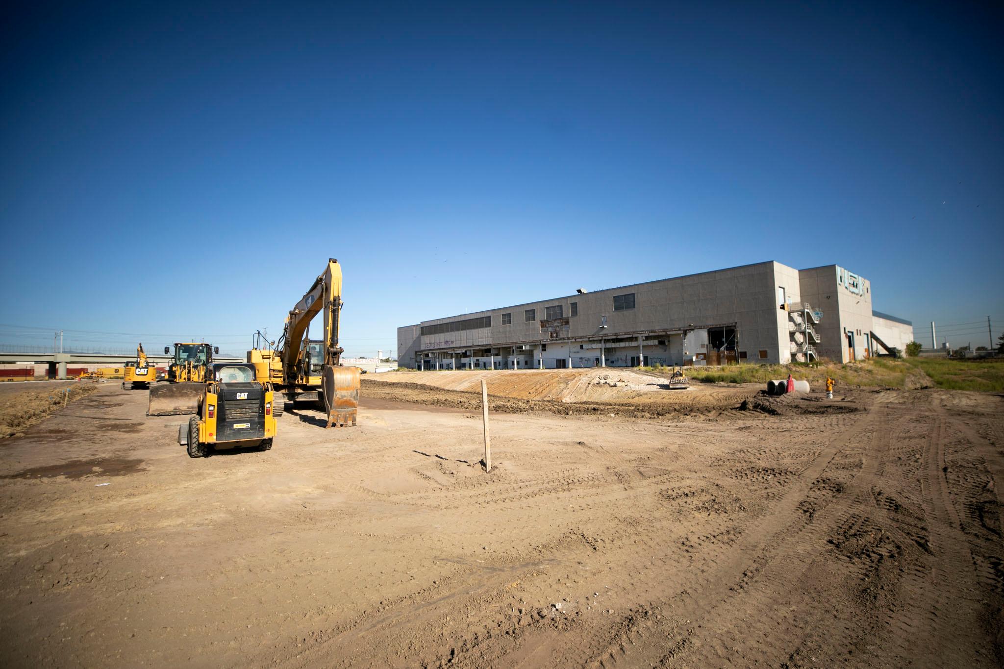 Yellow backhoes and bulldozers sit on a dirt lot, populated only by a grey concrete building.