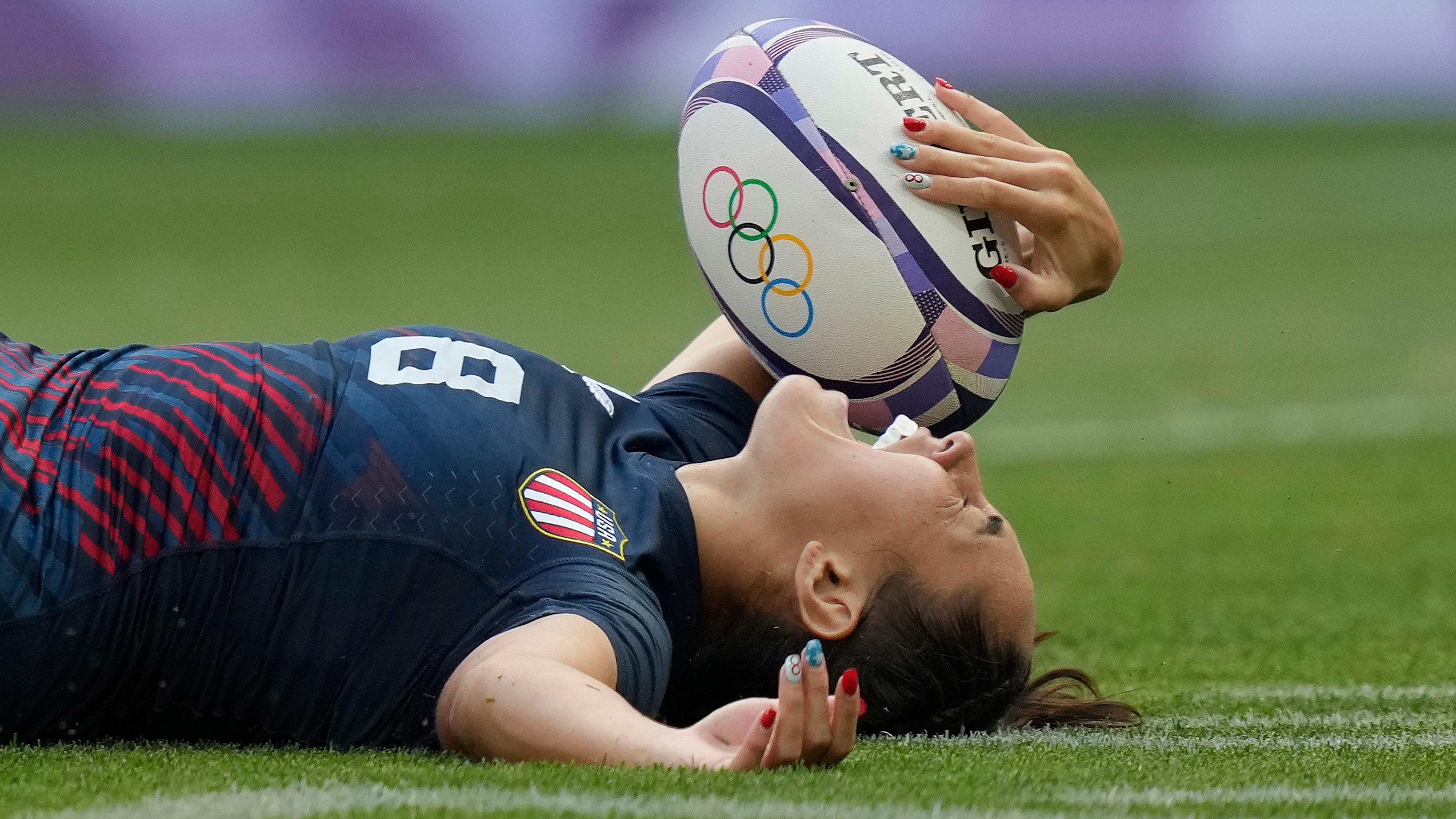 U.S. rugby player collapses on the grass, ball in hand, screaming in excitement after scoring the winning try during the women's bronze medal match.