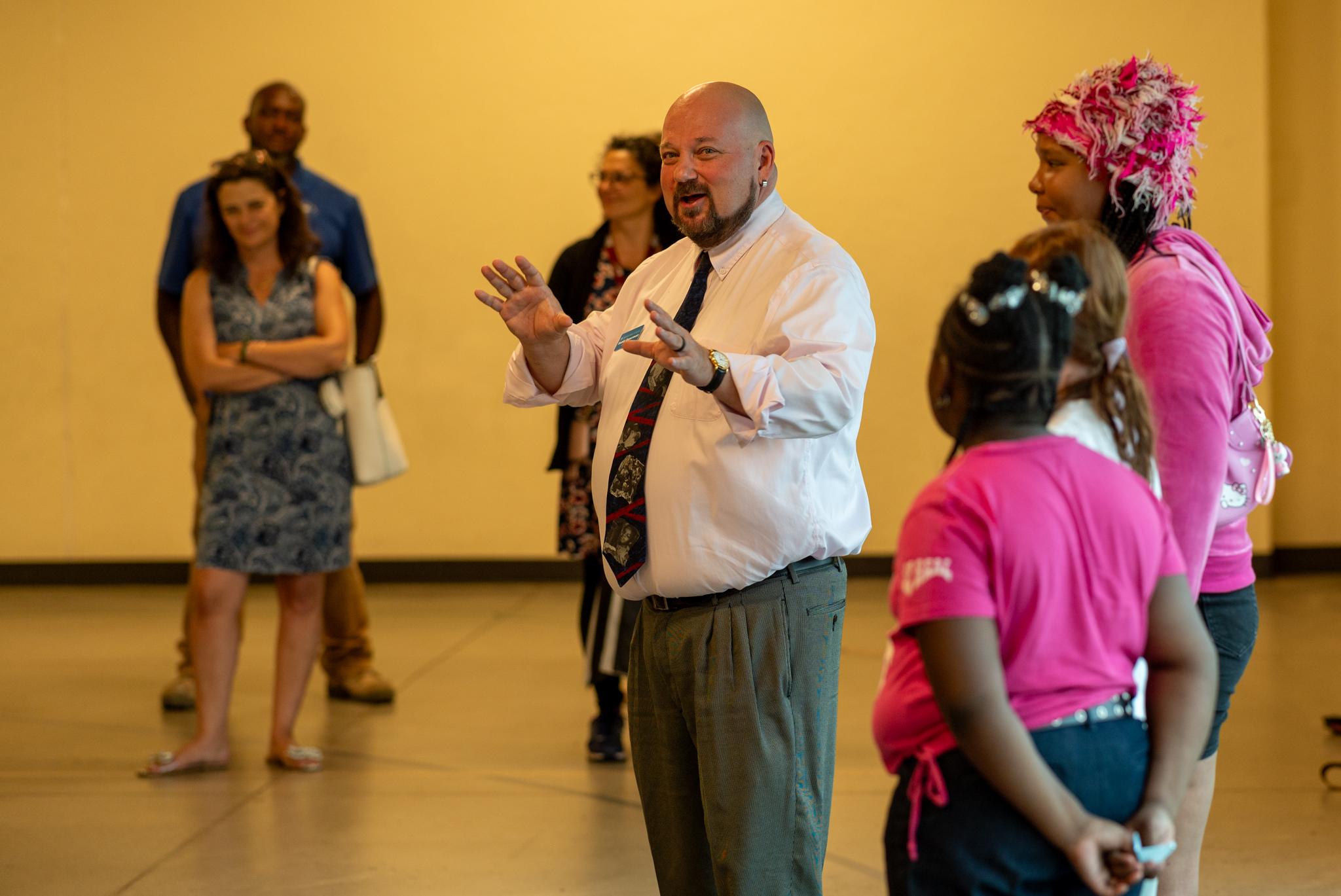 A group of adults and children stand indoors at an event celebrating the opening of the yurt.