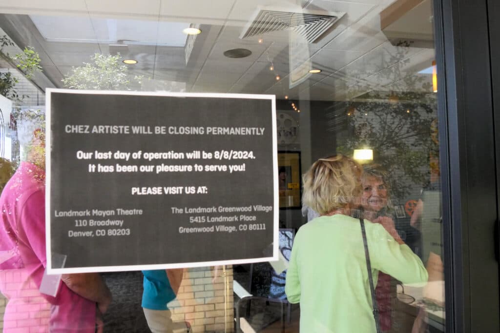 A sign posted to the entrance of the Chez Artiste, announcing the permanent closure of the theatre. An older crowd is lined up inside, waiting to buy tickets.