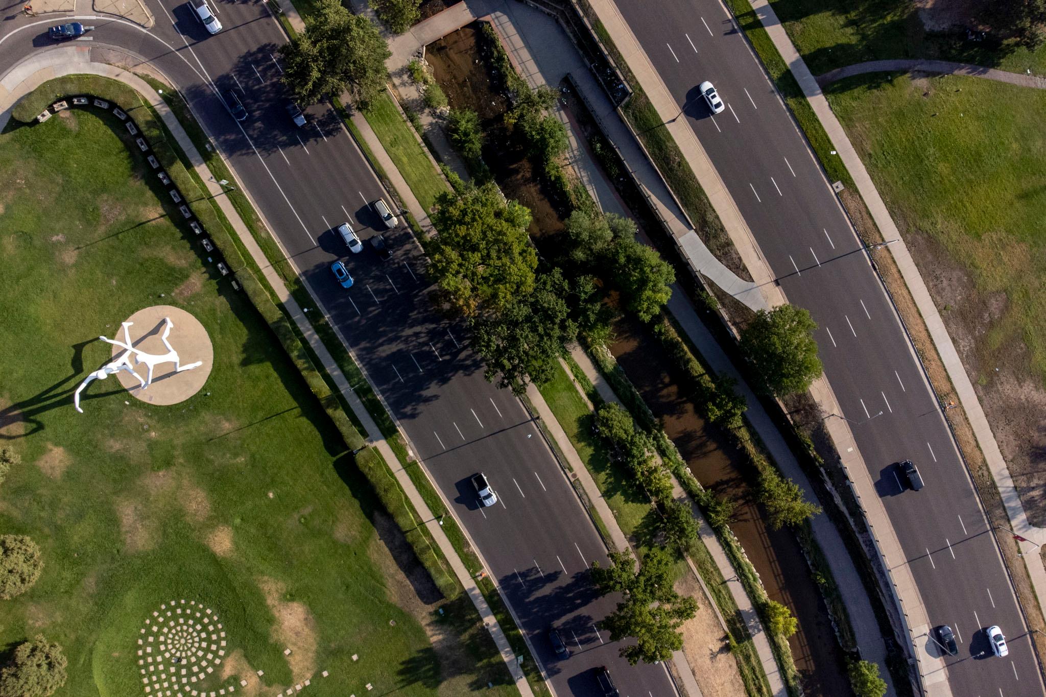 A top-down view of nine lanes of traffic, with a creek running between them; cars drive along the asphalt.