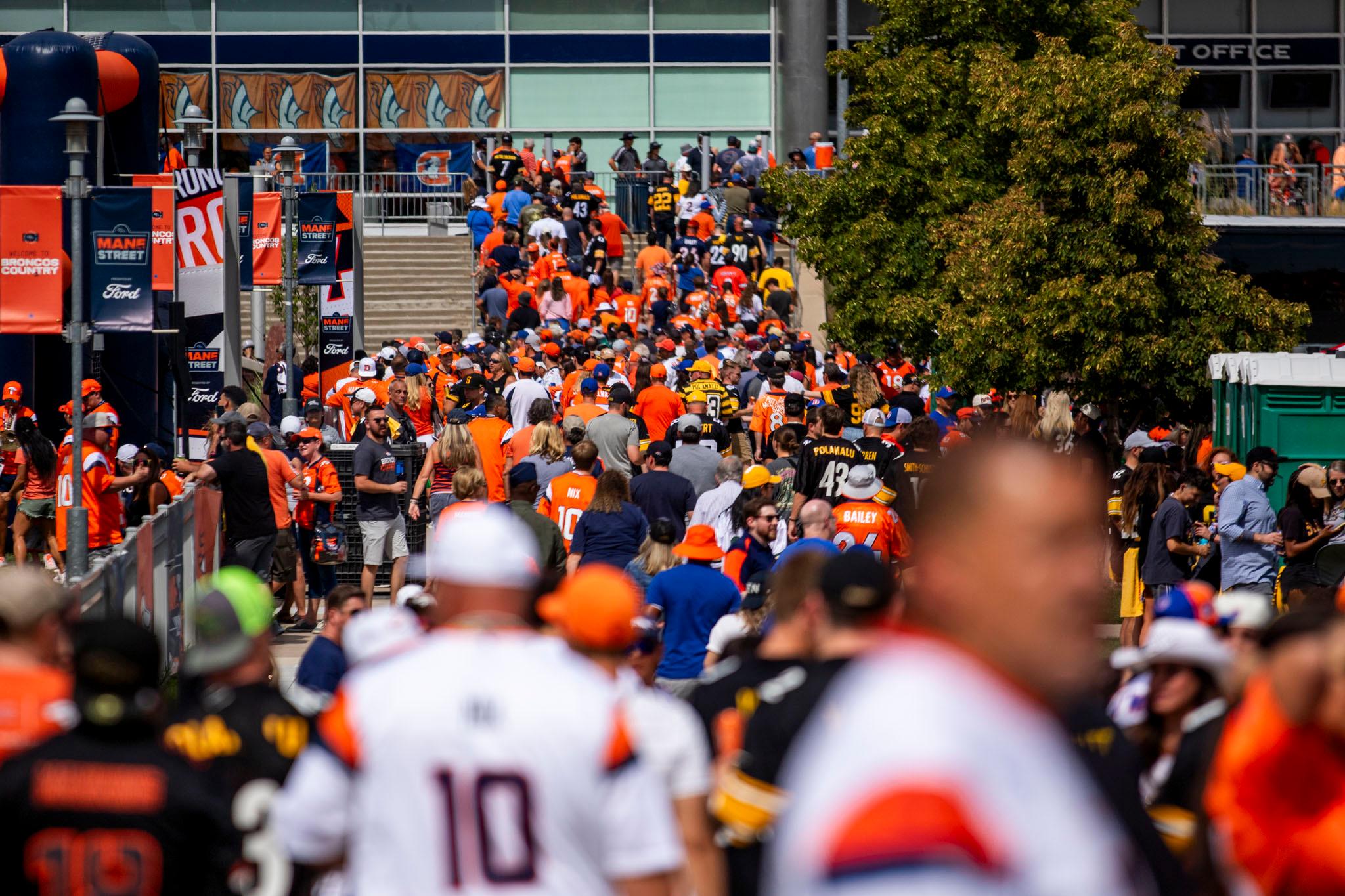 Hundreds of people line up to climb steps towards a stadium. They're an ocean of orange and blue.