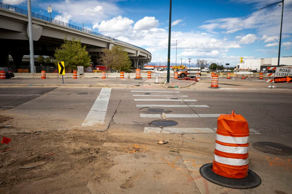 Construction cones surround a crosswalk; a highway lines the horizon behind it.