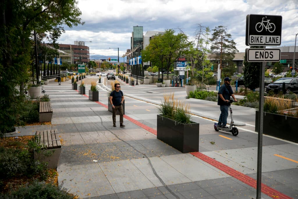 A view down Larimer Street, with Speer Boulevard signs and rope lights partially blocking a view of the mountains beyond; people walk and scooter by in the foreground.