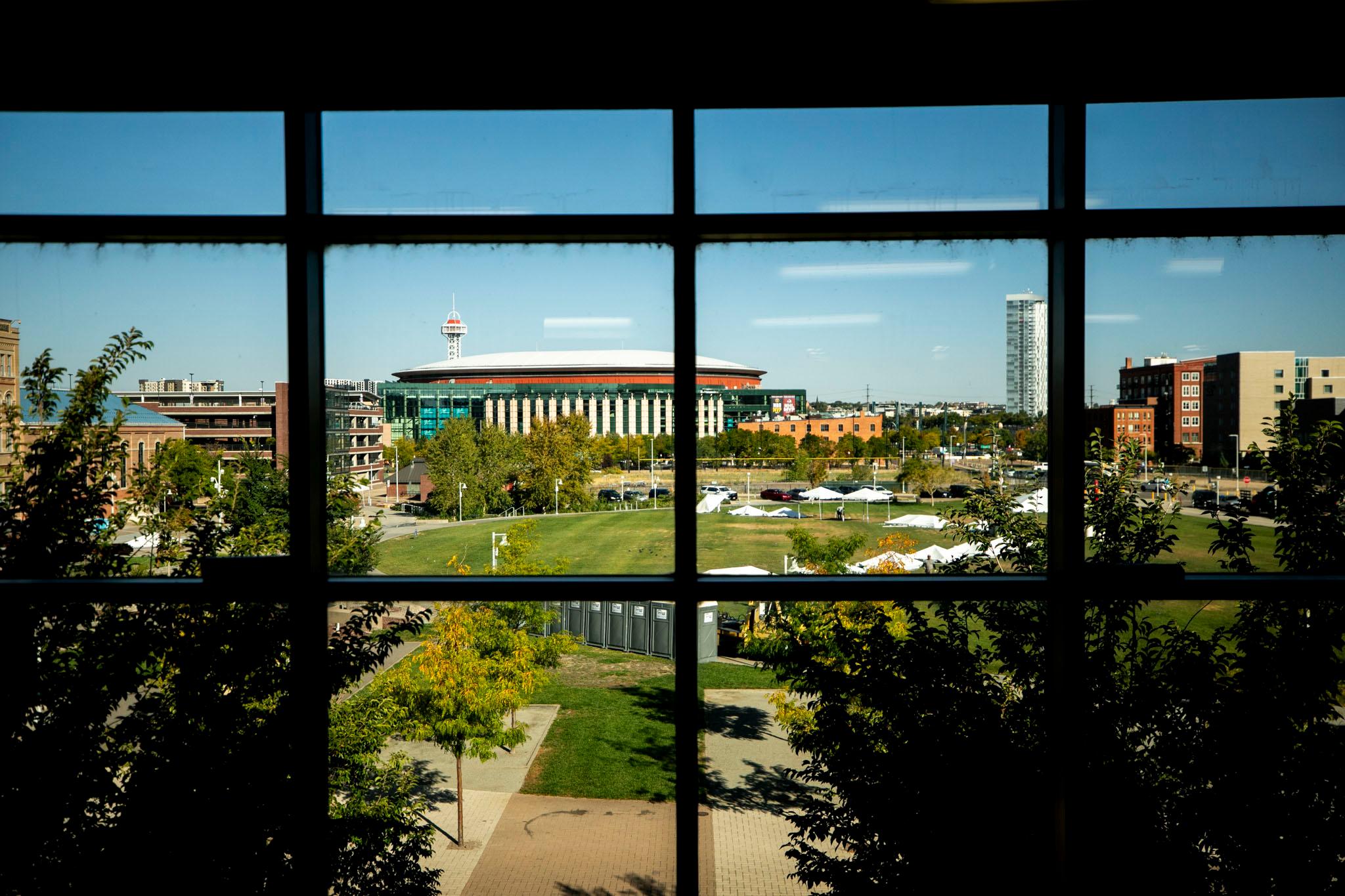 Ball arena can be seen through the silhouetted grid of a window in the foreground, surrounded by blue skies and green lawns.