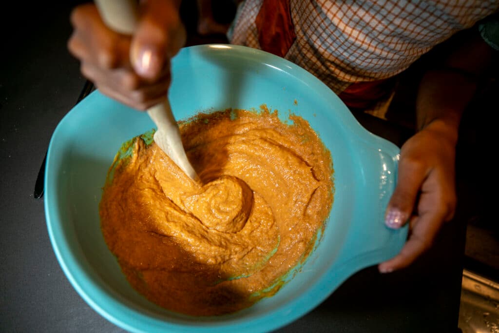 A top-down shot of a bowl filled with orange paste, swirling as a girl's hands direct a spoon in circles inside.