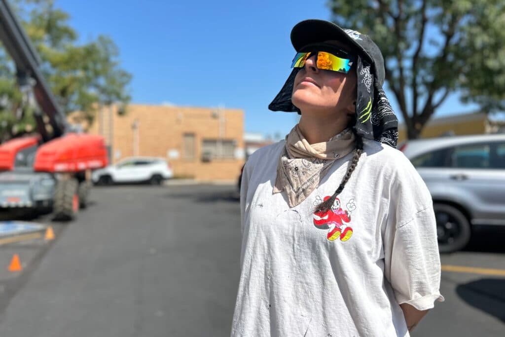 A woman dressed in a white t-shirt and wearing mirrored sunglasses is seen staring at a mural, reflected in her glasses.