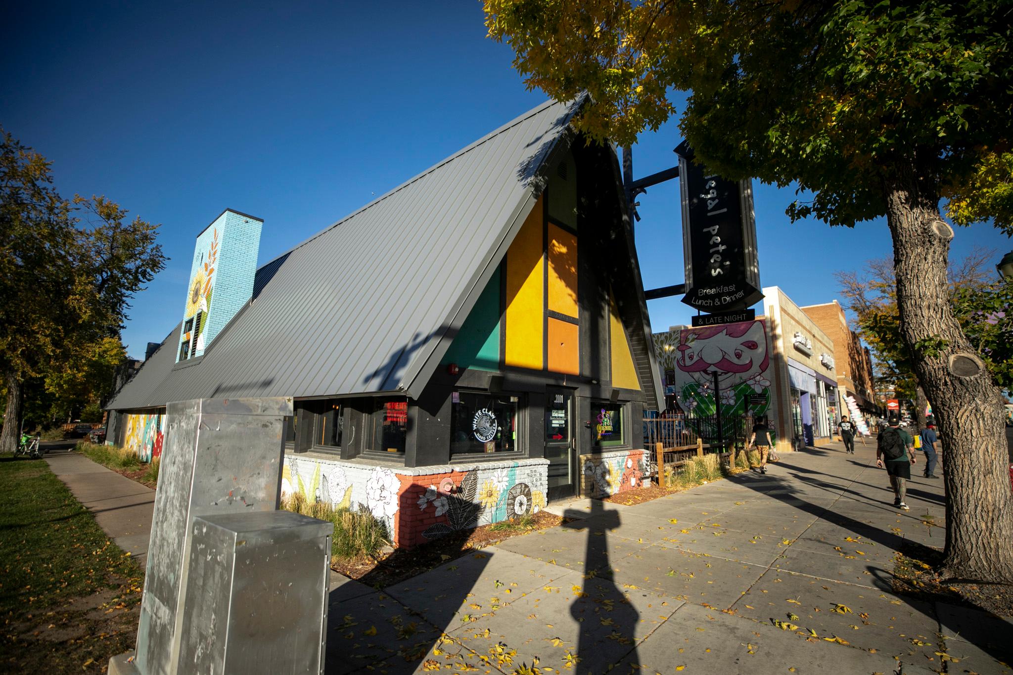 An A-frame building adorned with splashes of orange, green and yellow. It's all blue skies above.