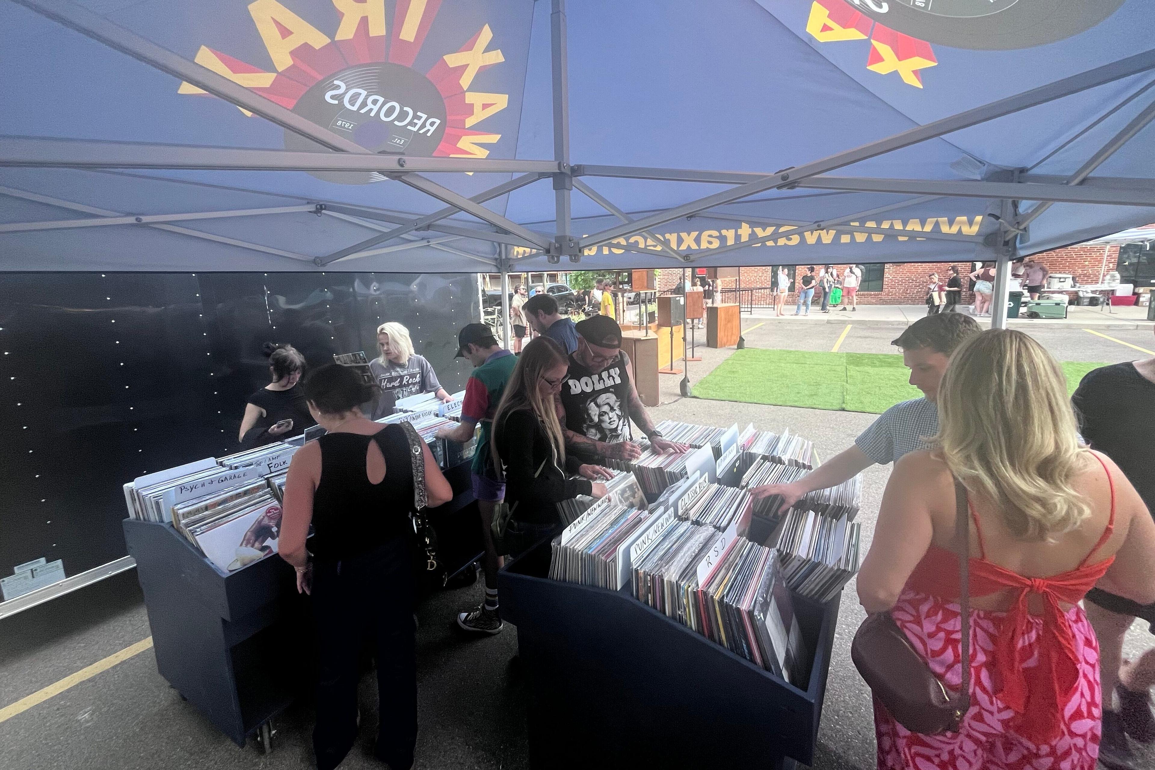 People browse through records outdoors under a shade canopy at a Wax Trax Records pop-up.