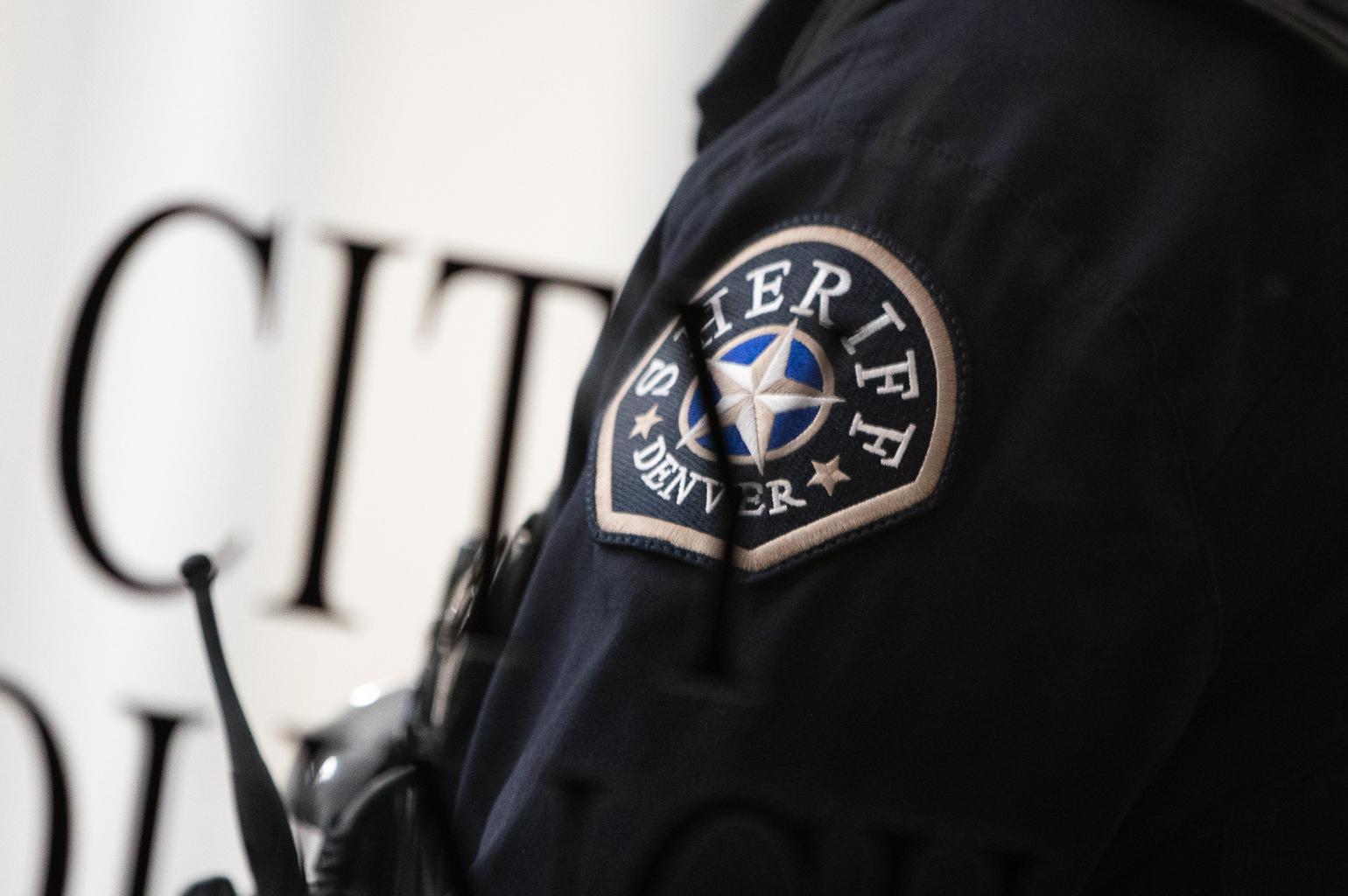 A Denver Sheriff deputy stands beside the glass door to Denver City Council chambers.