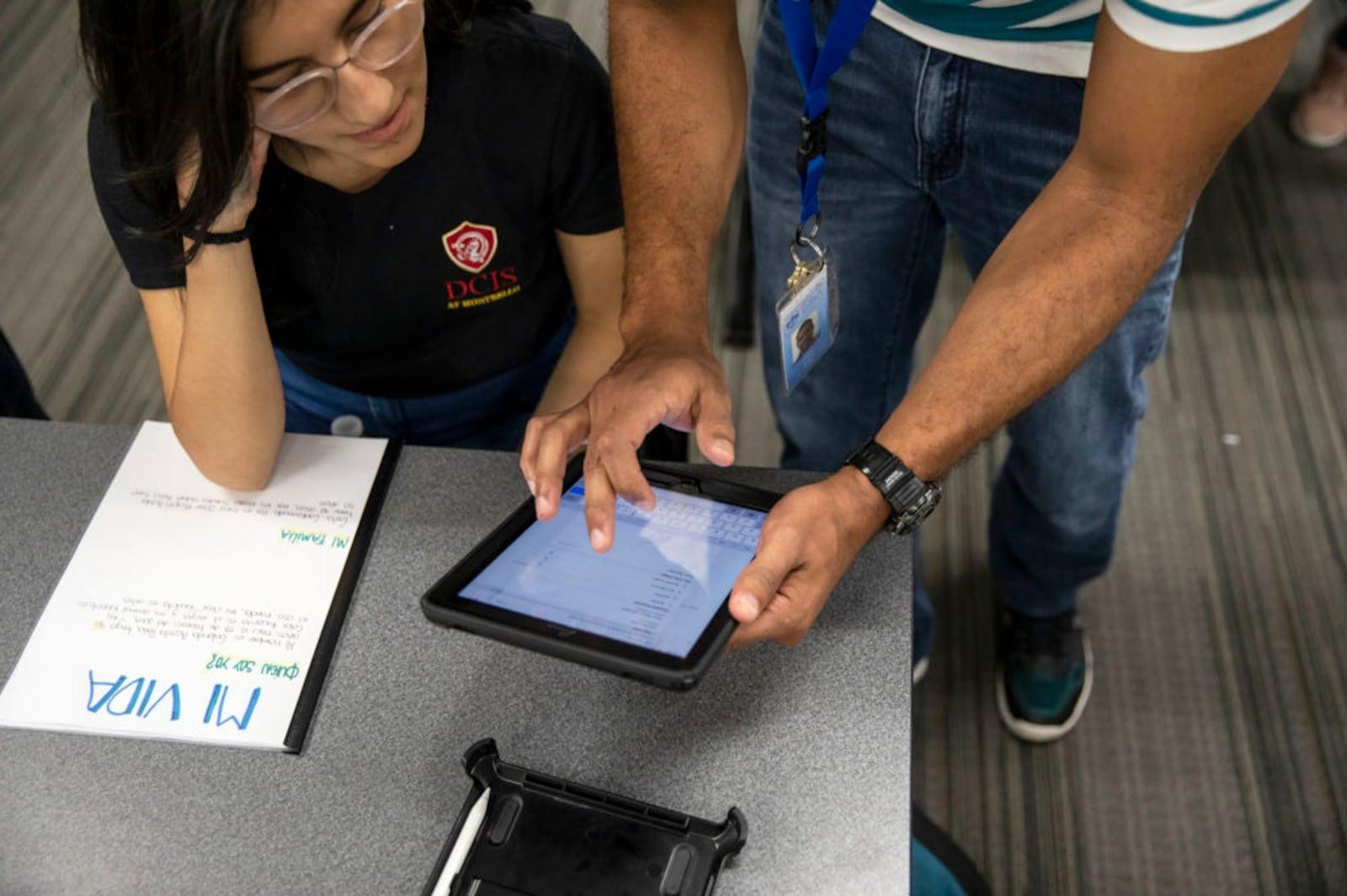 Teacher with an iPad speaks to a student at her desk