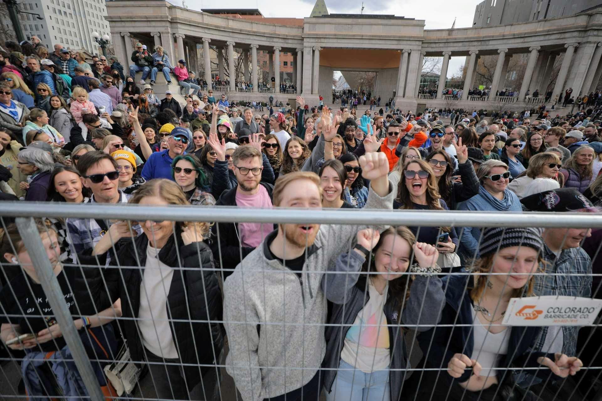 A large crowd of people raise their fists and wave at a camera.