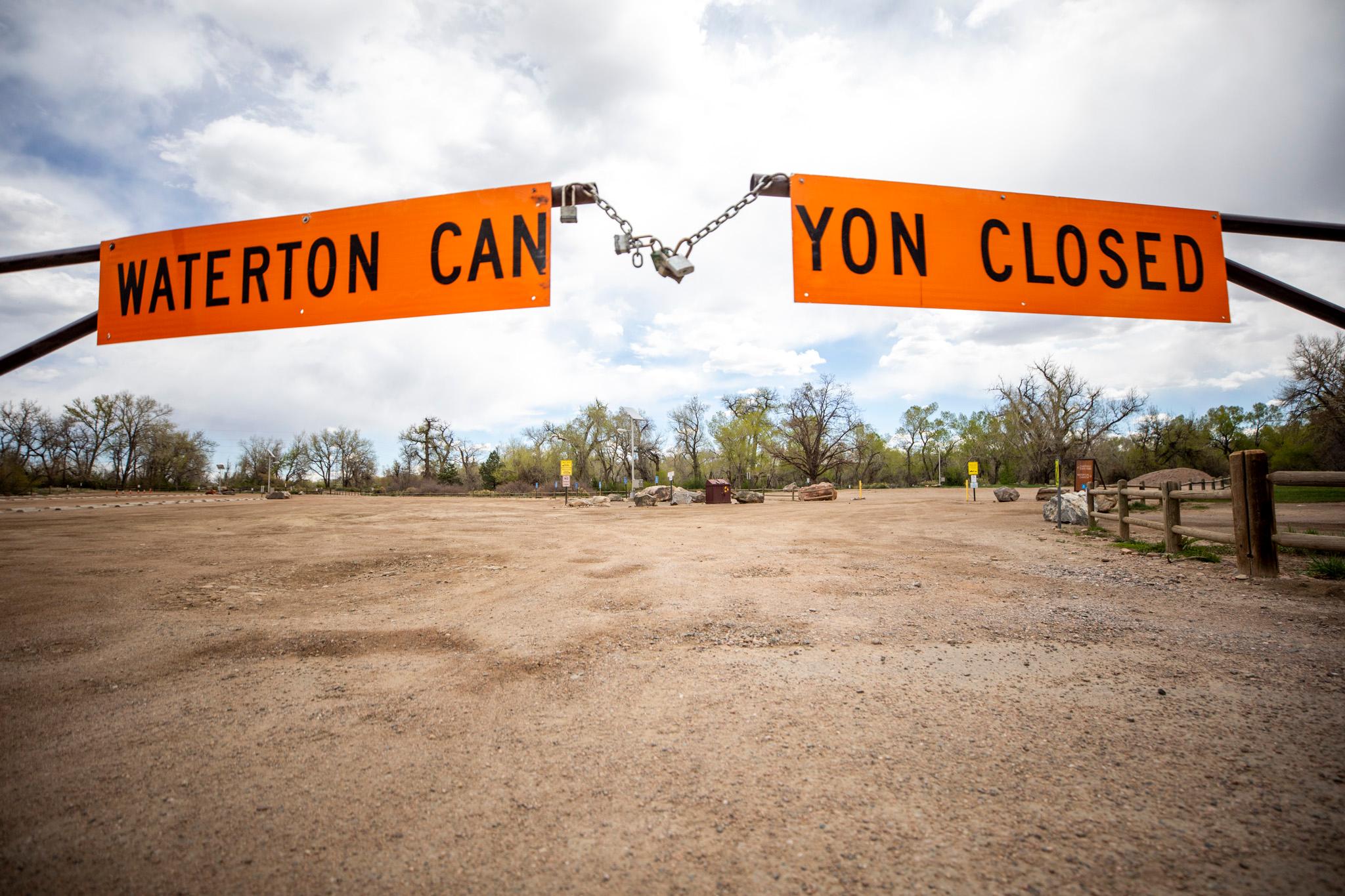 Two orange signs on a metal gate read "WATERTON CANYON CLOSED," split down the middle of the phrase. A lock hangs between them.