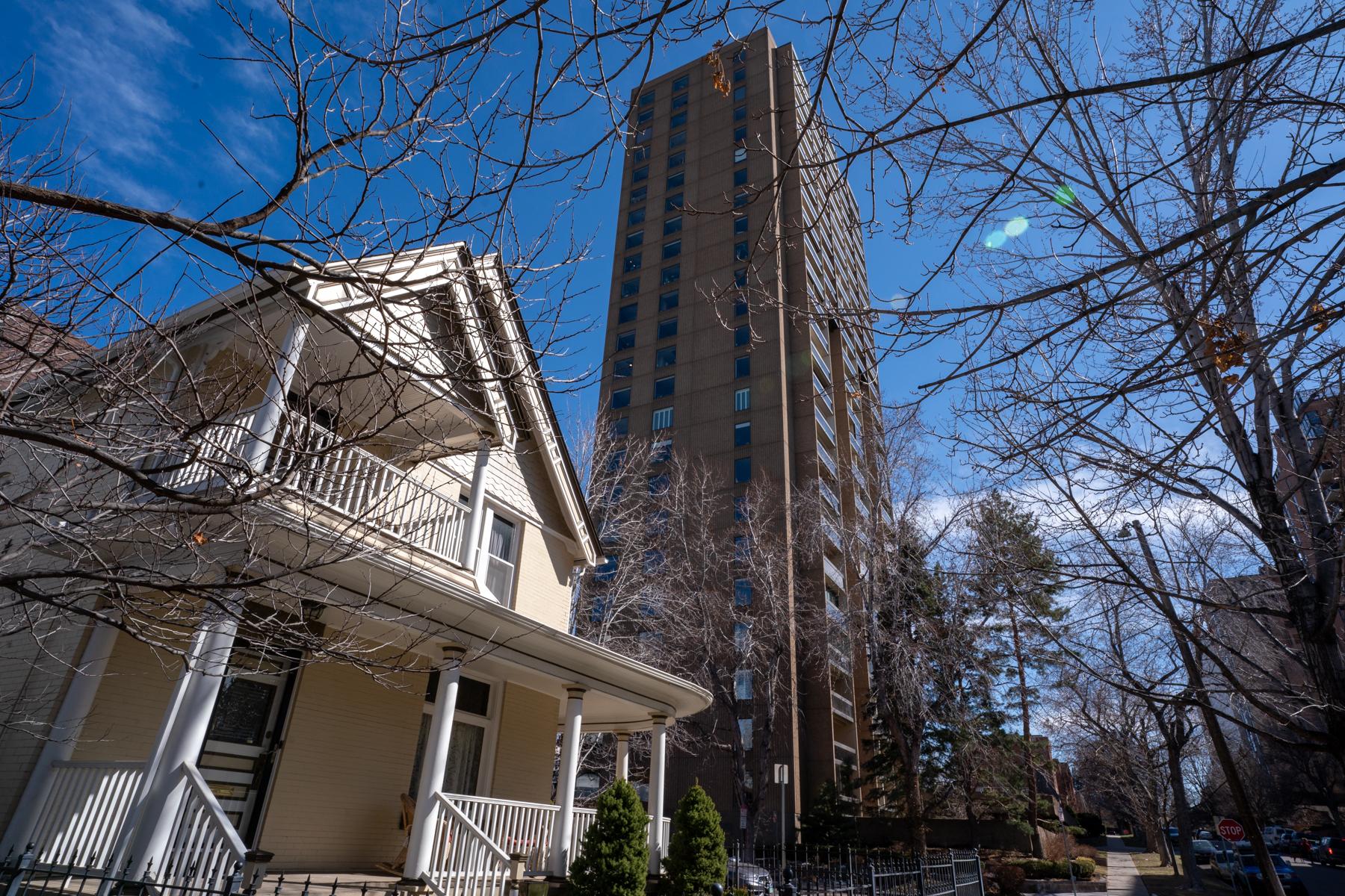 A very tall reddish apartment building in the background towers over a yellow single-family home in the foreground.