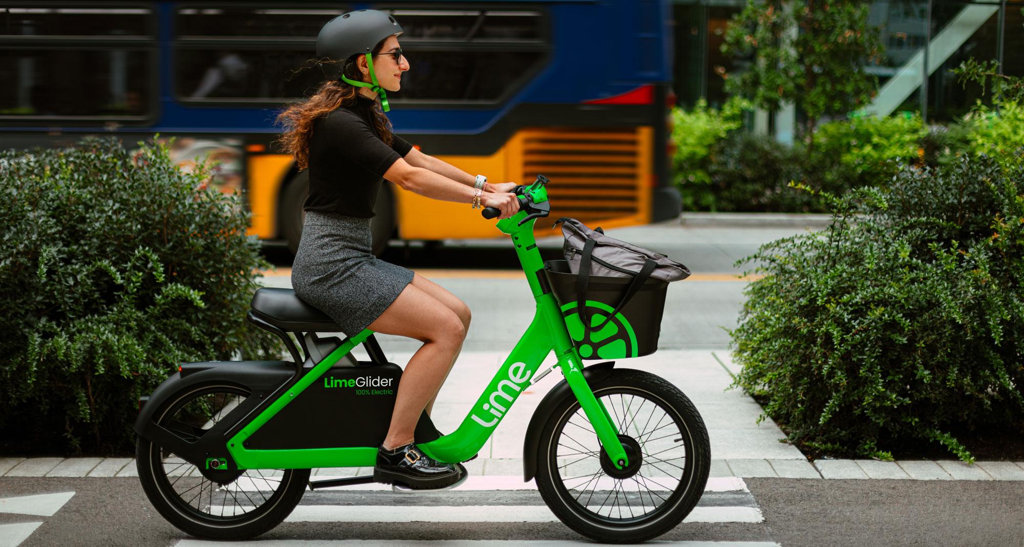 A woman rides a green vehicle that resembles a bike but has no pedals.