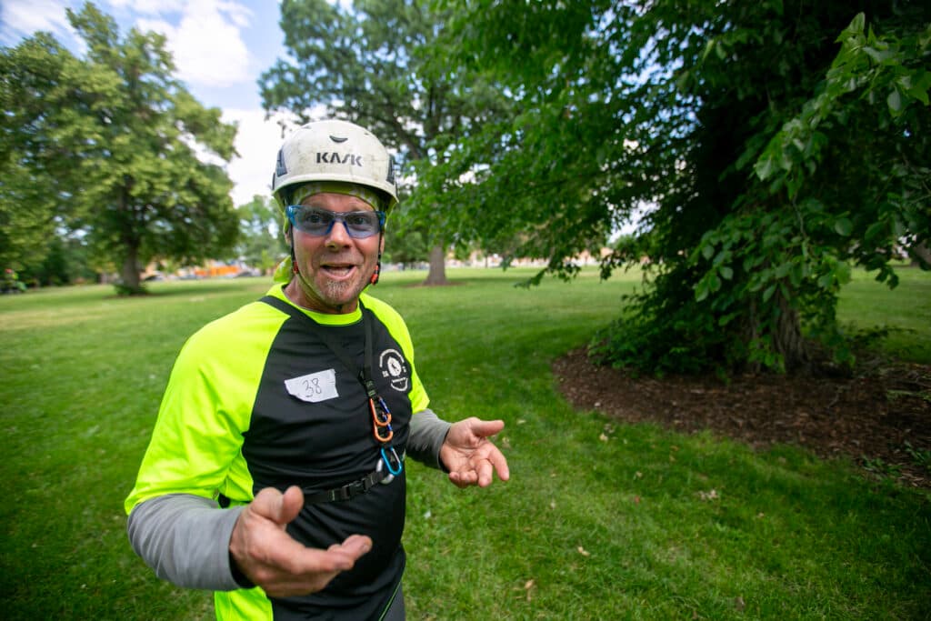 Patrick O'Meara gesticulates as he speaks, dressed in helmet, safety glasses, and vibrant green/yellow shirt.