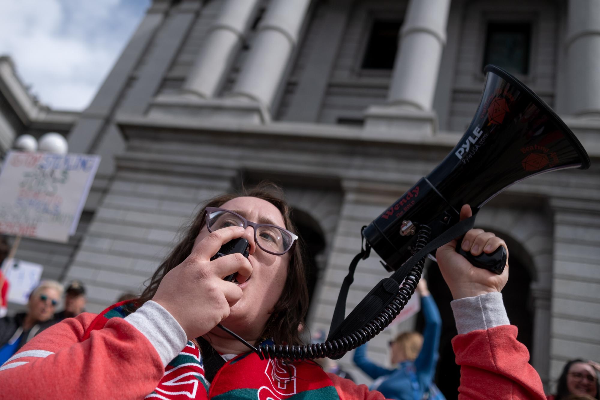 A woman speaks into a megaphone with the state Capitol building behind her.