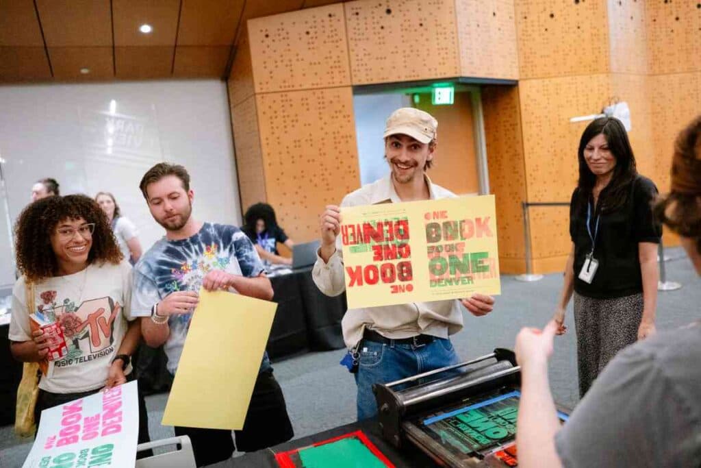 Several people crowd around a printing station at an event some hold up posters they made