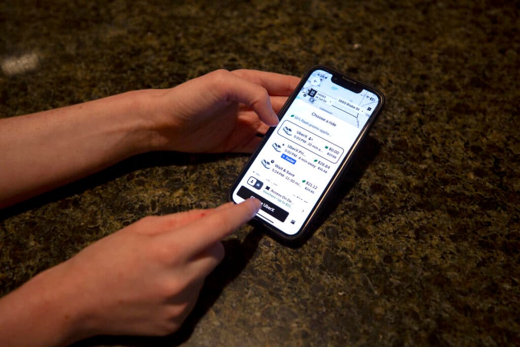 A close-up on a phone, with a pair of hands coming from the left side of the frame. One points to the screen, an Uber pickup menu with one option that reads $0.00.