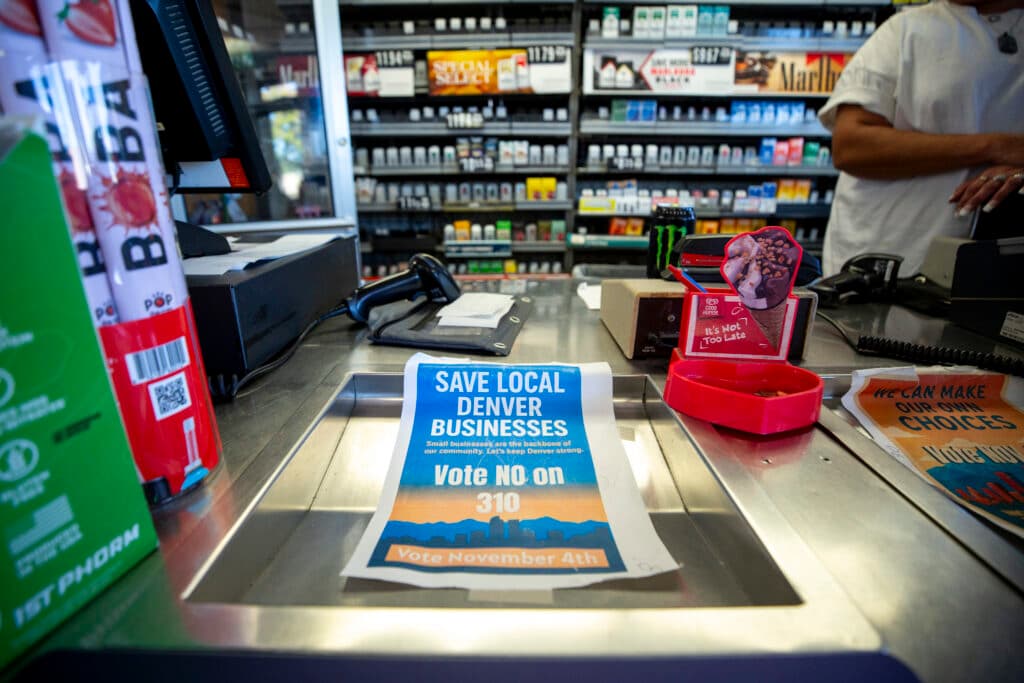 A counter with a blue sign on it that reads "SAVE LOCAL DENVER BUSINESSES; BOTE NO ON 310."