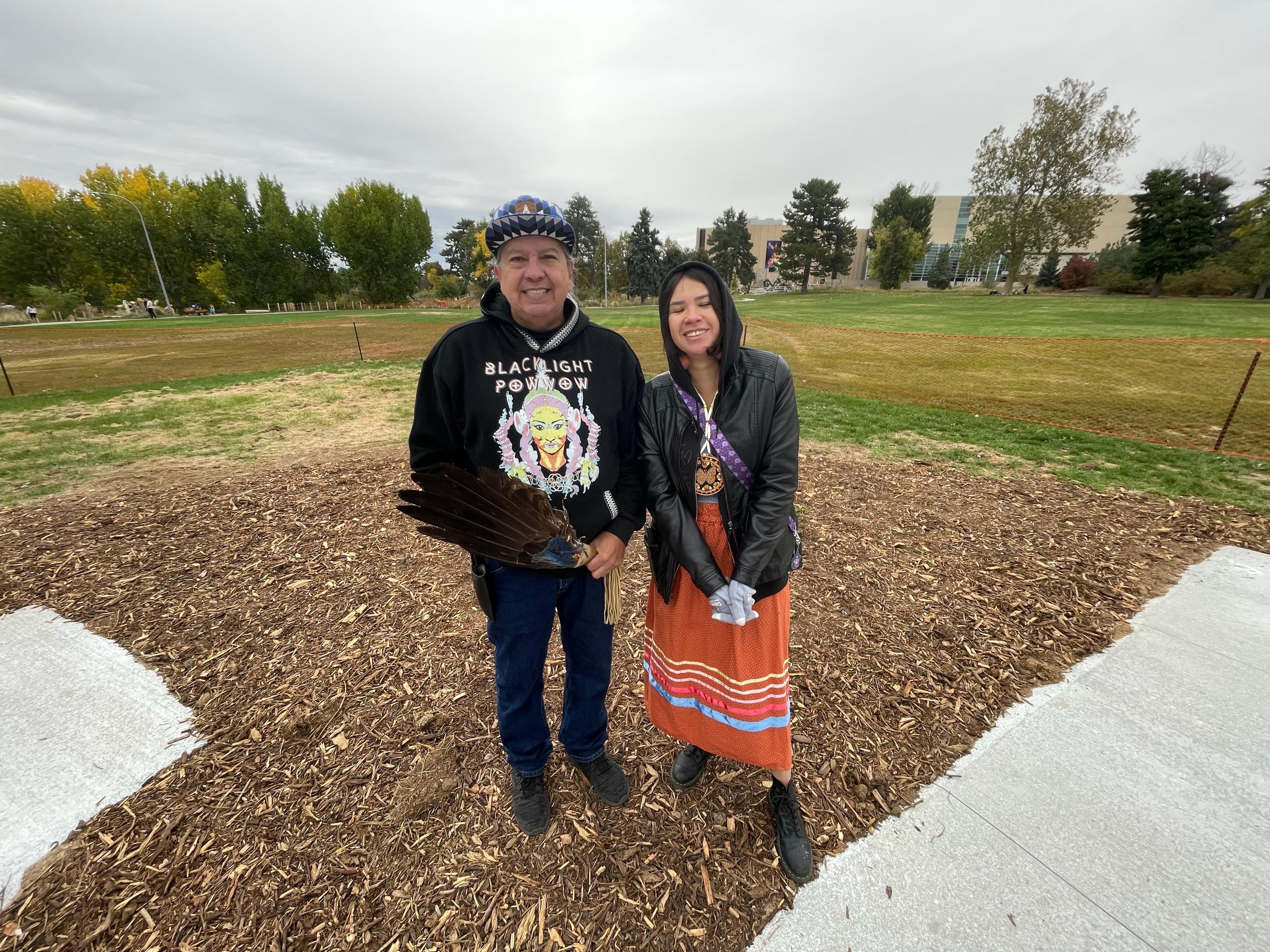 Sid Whiting and Kristina Maldonado Bad Hand stand in front of a field in front of the Denver Museum of Nature and Science at City Park.