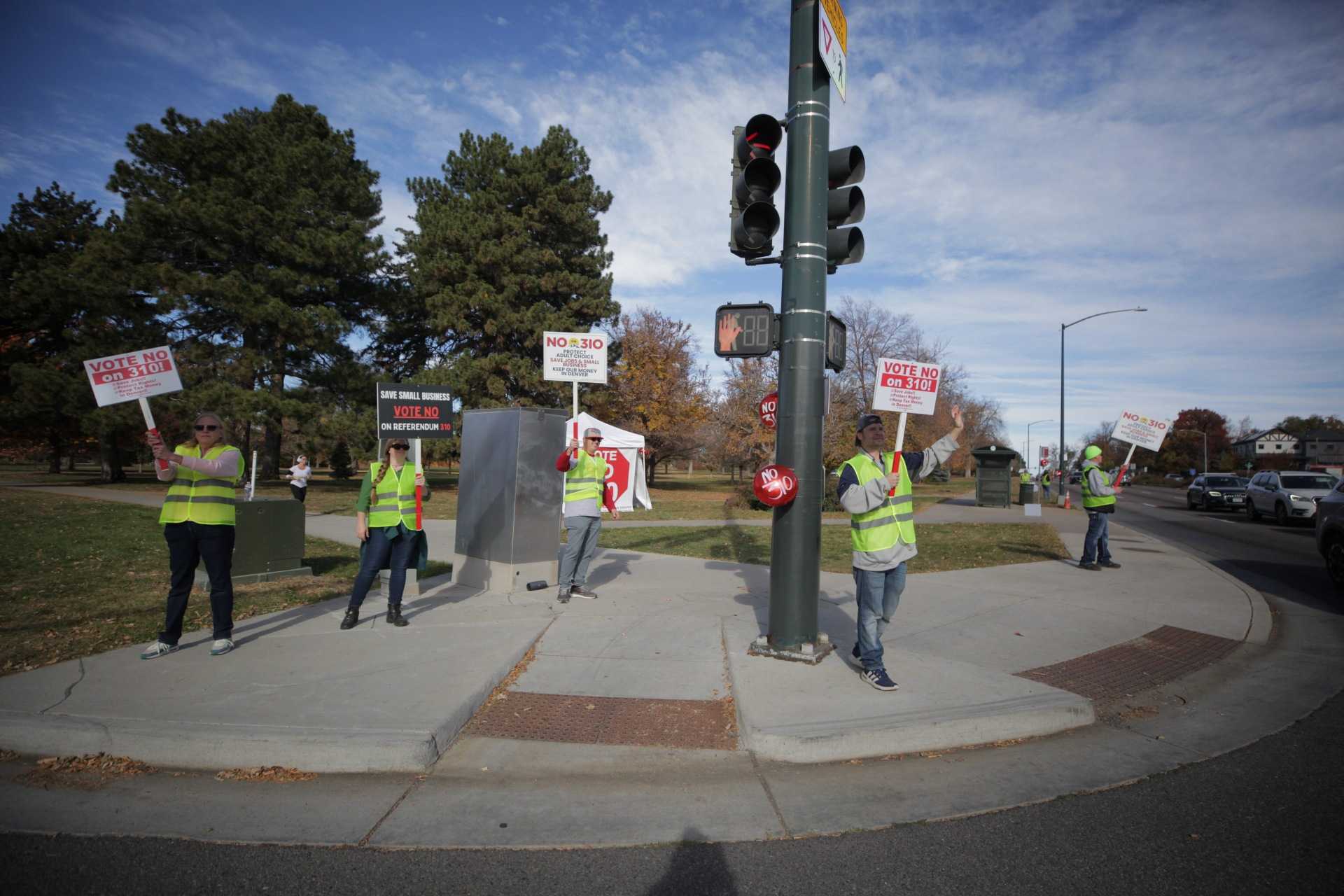 People in yellow safety vets hold &quot;No on 310&quot; signs on a street corner.